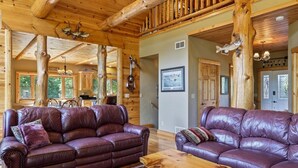 A cabin interior with two leather sofas, wooden flooring, and a dining area. - The Cabin at The Land of the Yellow River (Necedah)