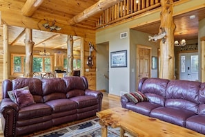 A cabin interior with two leather sofas, wooden flooring, and a dining area. - The Cabin at The Land of the Yellow River (Necedah)