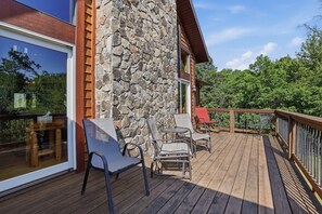 Une terrasse en bois avec des meubles d’extérieur, un mur en pierre et une vue sur les arbres.