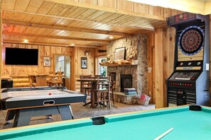A billiards room with a pool table, a dartboard, and a fireplace.