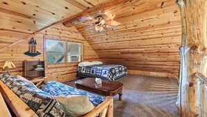 A cozy log cabin room with a loft bed, a sofa, a small table, and a ceiling fan. - The Cabin at The Land of the Yellow River (Necedah)