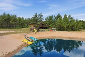 A swimming pool with boats, a wooden deck, and a house surrounded by trees. - The Land in the Pines-Cabin (Necedah)