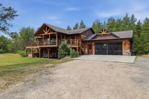 A two-story log cabin with a covered porch, a garage, and a gravel driveway.