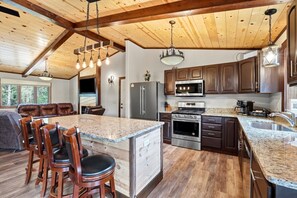 A spacious kitchen with granite countertops, stainless steel appliances, and a large island with bar stools. - The Land in the Pines-Cabin (Necedah)