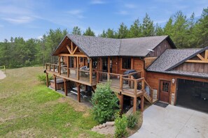 A two-story wooden cabin with a deck, a garage, and a landscaped yard.