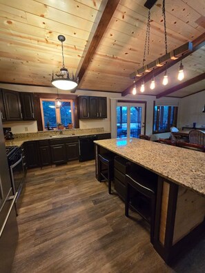 A modern kitchen with wooden ceiling beams, granite countertops, and dark cabinetry. - The Land in the Pines-Cabin (Necedah)