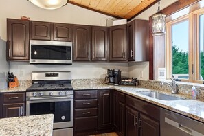 A kitchen with dark wooden cabinets, stainless steel appliances, granite countertops, and a window with a view of greenery.