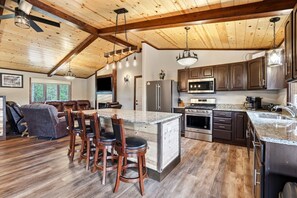 A spacious kitchen with a large island, dark wooden cabinets, stainless steel appliances, and a high ceiling with exposed beams. - The Land in the Pines-Cabin (Necedah)