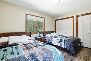 A room with two beds, a window, a nightstand, and a door. - The Land in the Pines-Cabin (Necedah)