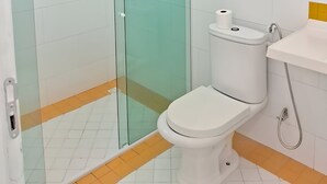 A bathroom with a glass shower enclosure, a white toilet, and a sink with a yellow-tiled backsplash. - Palladium Pousada (Neopolis)