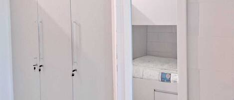 Un dormitorio con un armario blanco, una cama y un espejo en la pared.