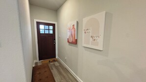 Un pasillo con un banco de madera, una puerta marrón y dos obras de arte en las paredes.