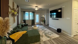 Una sala de estar moderna con un sofá verde, un televisor de pantalla plana grande y un espejo decorativo.