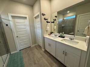 A modern bathroom with two sinks, a large mirror, and a shower.