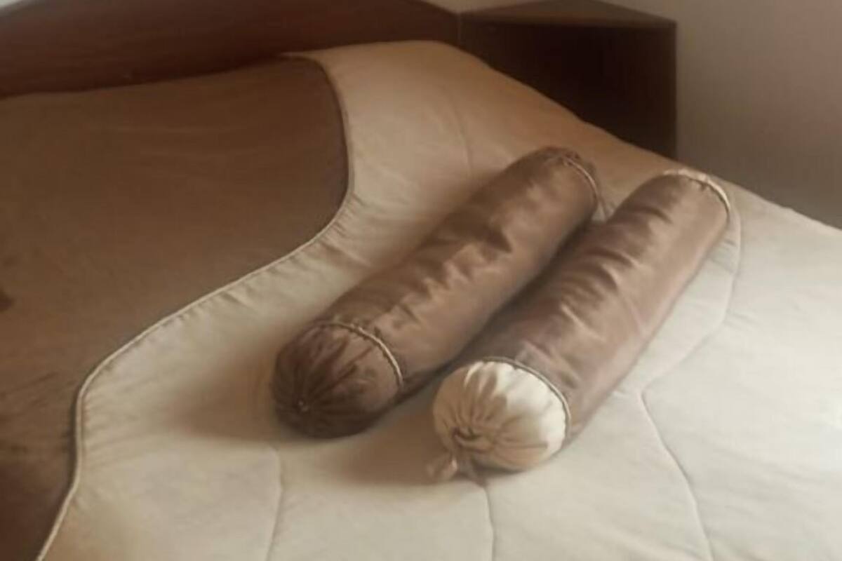 A bed with a beige and brown headboard, a small bedside table, and a plain wall.