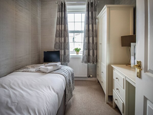 A bedroom with a bed, a TV, a dresser, and a window with curtains.