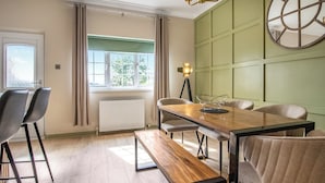 A dining area with a wooden table, four chairs, a bench, a floor lamp, and a window with curtains.