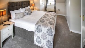 A bedroom with a large bed, a nightstand, a bedside lamp, a dresser, and a window with curtains.