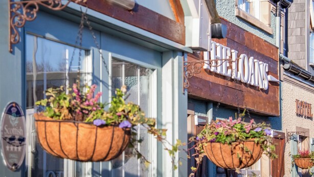 A hotel with a 'FREE LOANS' sign, large windows, and hanging flower baskets.