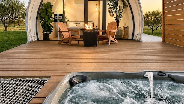 A dome-shaped structure with a hot tub, outdoor seating, and string lights.