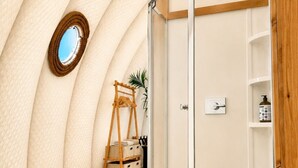 A room with a wooden floor, a glass shower enclosure, a wooden ladder, and a mirror on the wall.