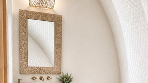 A bathroom with a wooden vanity, a large mirror, a round sink, a toilet, and a roll of toilet paper.
