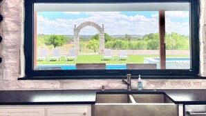 Eine Küche mit einer Steinwand, einem Fenster mit Blick auf einen Außenpool und Liegestühle, sowie einem integrierten Spülbecken.