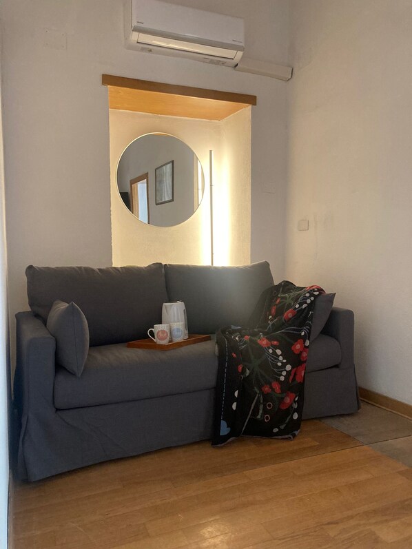 A modern living room with a grey sofa, a coffee table, a round mirror, and a floral throw blanket. - Evaref House (Naples)