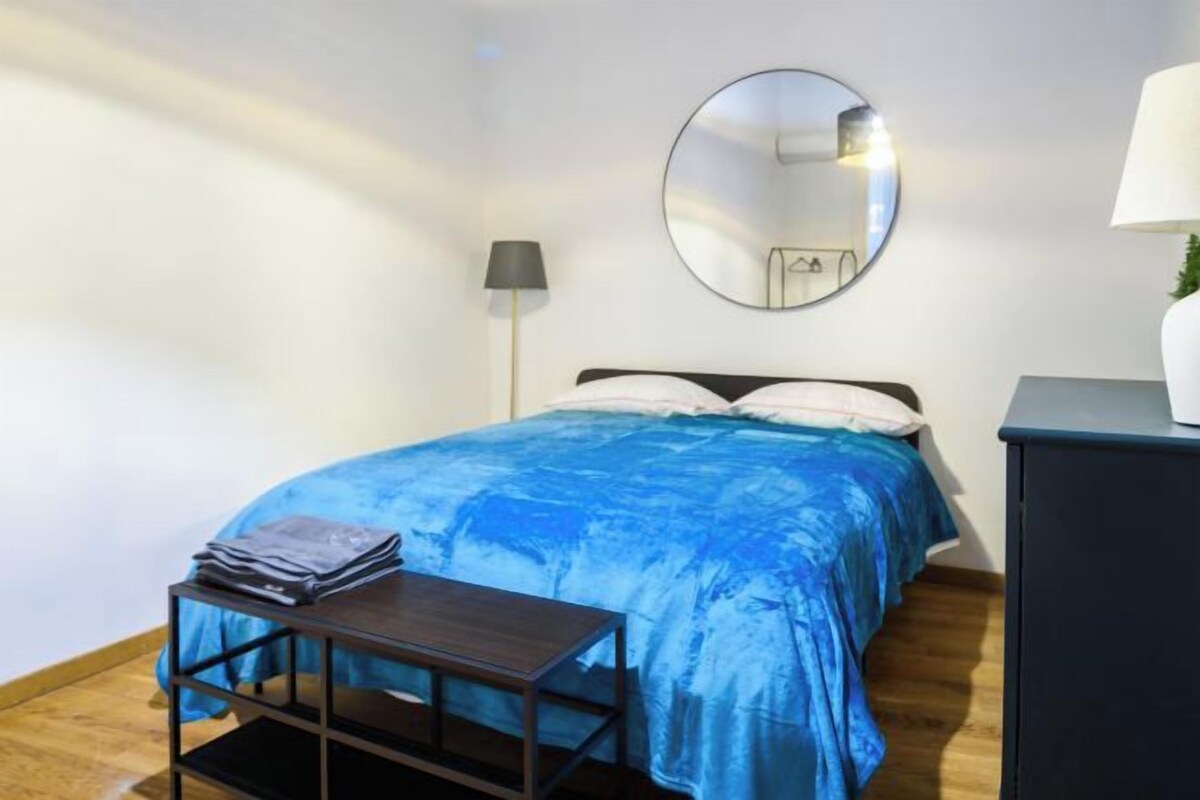 A bedroom with a bed, a bedside table with a lamp, a mirror, and a dresser.