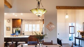 A spacious dining area with a wooden table and chairs, a hanging light fixture, and a view into the kitchen.
