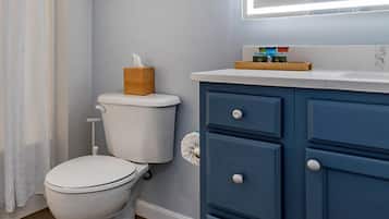 Un baño con inodoro blanco, un mueble azul con cajones y un espejo sobre el lavamanos.