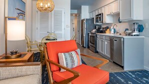 A modern living room with a bright orange chair, a dining area with a glass table, and a kitchen with stainless steel appliances. - Carolina Grande (Myrtle Beach)