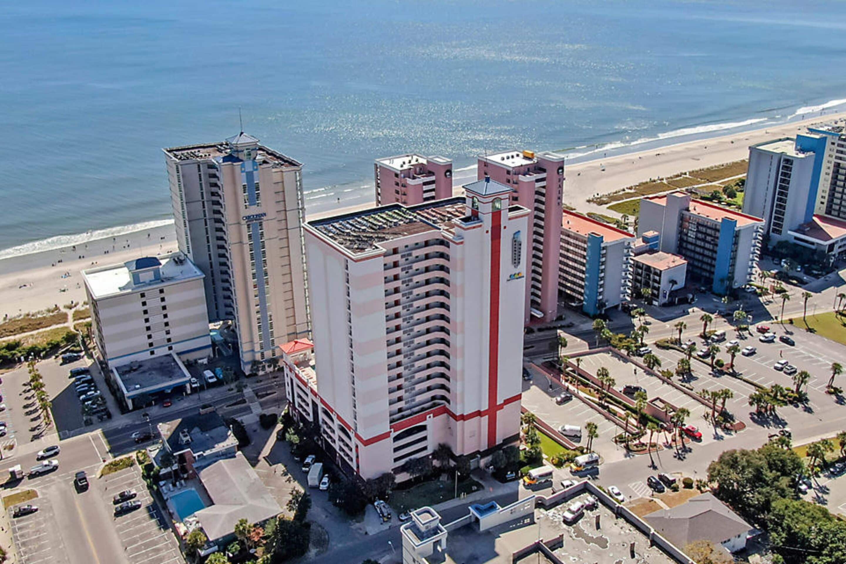 A high-rise hotel with multiple floors, a rooftop pool, and a view of the beach.