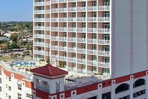 Et hotel med flere etager, altaner, et poolområde på taget og en bygning med rødt tag.
