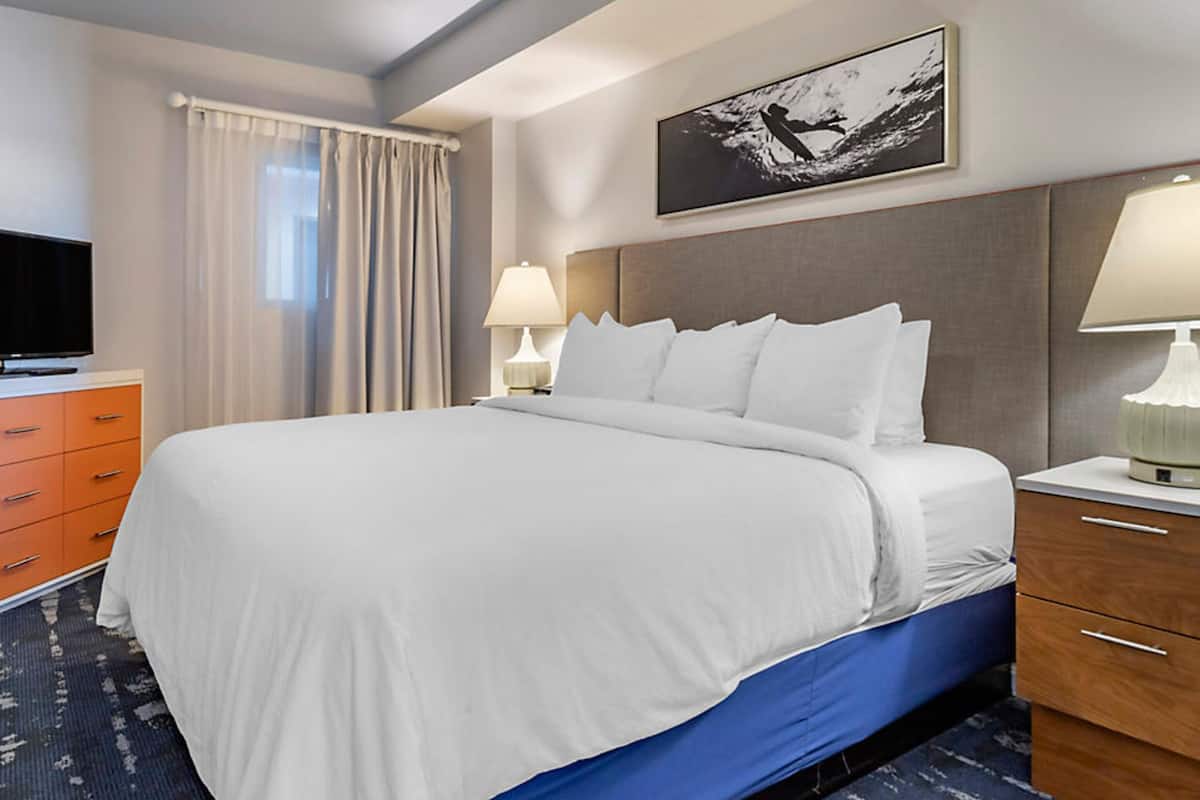 A hotel room with a large bed, a television, a desk with a lamp, and a painting on the wall.