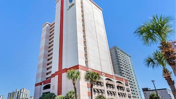 A tall hotel with multiple floors, a prominent red and white facade, and several palm trees in front.