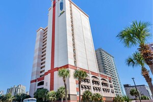 Un hotel alto de varios pisos, con una llamativa fachada roja y blanca y varias palmeras frente a él.