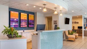 A reception area with a curved counter, a large wall with three sunset paintings, and a seating area with two chairs and a plant. - Carolina Grande (Myrtle Beach)