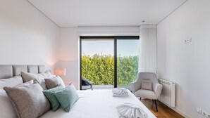 Ein modernes Hotelzimmer mit einem großen Bett, einem Sessel, Blick auf Grünflächen und einer Heizung.