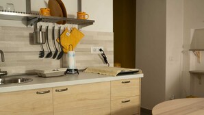 A kitchen with a sink, countertop, and wooden cabinets. There are utensils hanging on the wall and a coffee mug on the shelf. - Vesuvio Home Capodichino Blue (Naples)