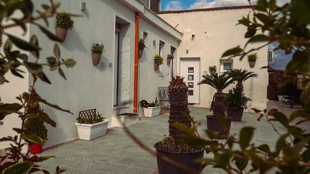 A courtyard with potted plants, a tiled floor, and a building with a white facade and red accents. - Vesuvio Home Capodichino Blue (Naples)