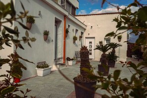 A courtyard with potted plants, a tiled floor, and a building with a white facade and red accents. - Vesuvio Home Capodichino Blue (Naples)