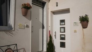 A building entrance with a white door, a small potted plant on the wall, and a window with a metal frame. - Vesuvio Home Capodichino Blue (Naples)