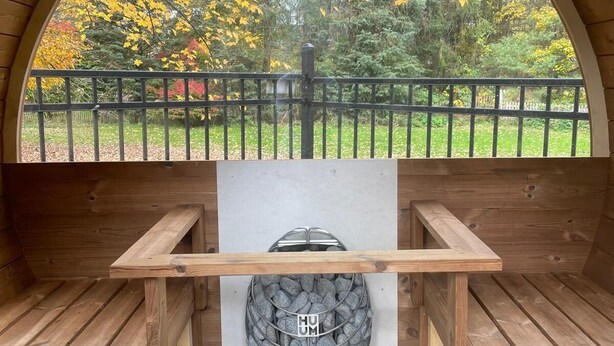 Een houten constructie met een rondboogvenster dat uitkijkt op een tuin met geel herfstblad.