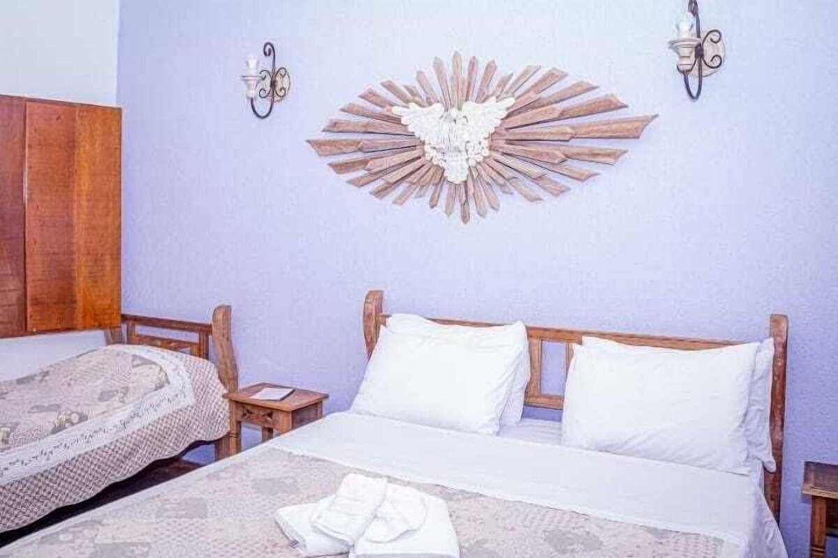 A bedroom with two beds, a decorative wall piece, and two wall sconces.