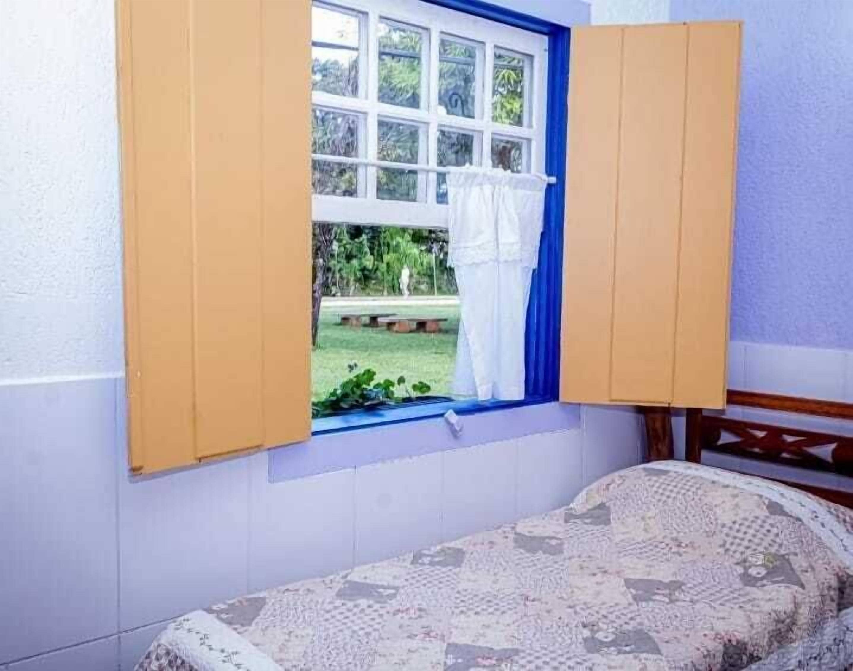 A room with a bed, a window with curtains, and a view of a garden.