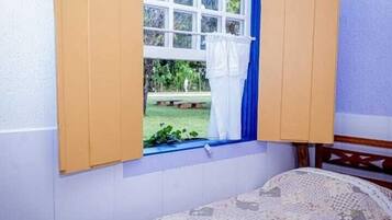 A room with a bed, a window with curtains, and a view of a garden.