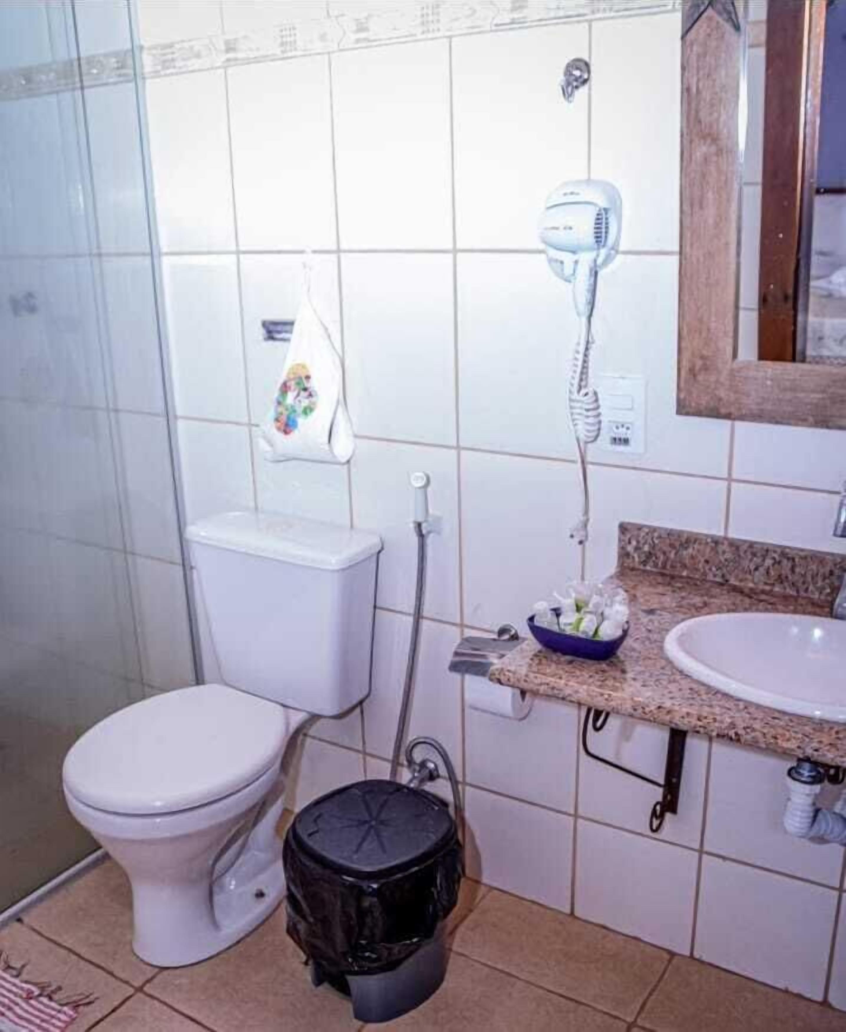 Une salle de bain équipée de toilettes, d’un sèche-cheveux, d’un lavabo et d’une poubelle.