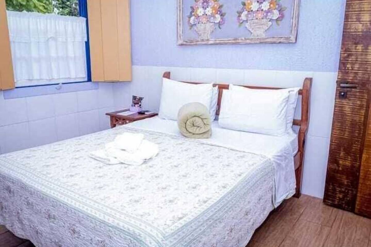 A neatly made bed with a patterned bedspread, a clock, and pillows.