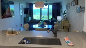 Eine moderne Küche mit einer großen Kochinsel, ein Essbereich mit Tisch und Stühlen sowie ein Wohnzimmer mit Sofa und Fernseher.